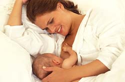 Женщина кормит малыша грудью лежа на кровати